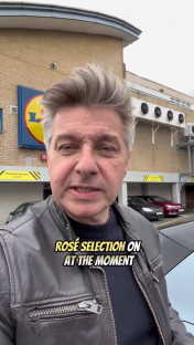 Man in leather jacket outside Lidl reviewing rosé selections.