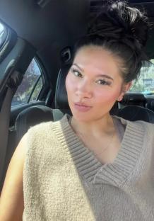 Woman in a car, wearing a tan sweater.