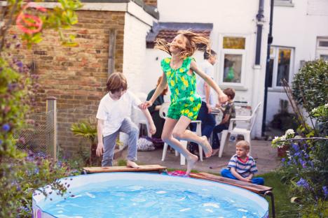 Girl jumping into a paddling pool in a garden.