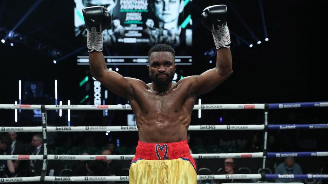A victorious boxer raises his arms in the ring.