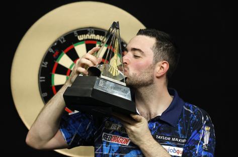 Luke Humphries kissing a darts trophy.