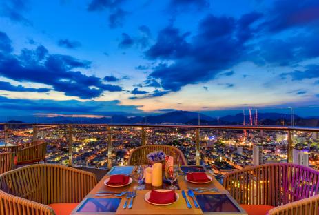 Romantic rooftop dinner setting overlooking a city at sunset.