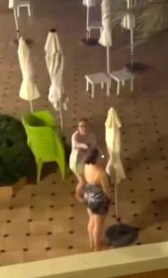 Video grab of two women retrieving towels from sunbeds at a hotel pool at night.