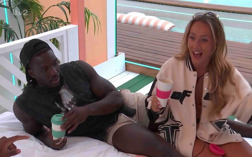 Two people relaxing on a bed, each holding a reusable coffee cup.