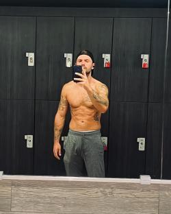 Shirtless man taking a selfie in a gym locker room.