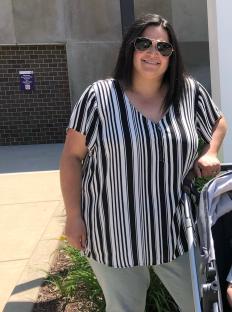 Woman in black and white striped shirt standing outdoors with a stroller.