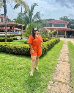 Woman in orange jumpsuit standing on a lawn.