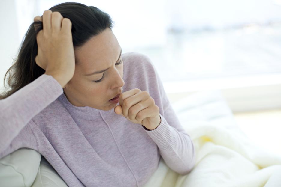 Young woman coughing into her fist while holding her head with the other hand.