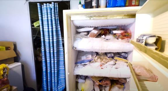 Overstuffed freezer with frost and various frozen food items.