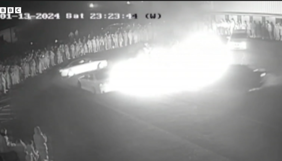 CCTV footage shows a car on fire with a crowd of people watching.