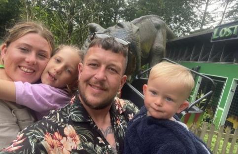 Family selfie with two children in front of a dinosaur.