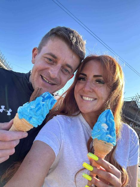 A man and a woman smiling and holding blue ice cream cones.