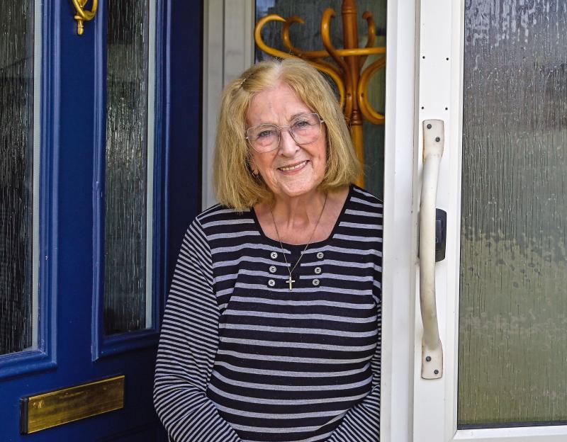 A smiling older woman stands in her doorway.