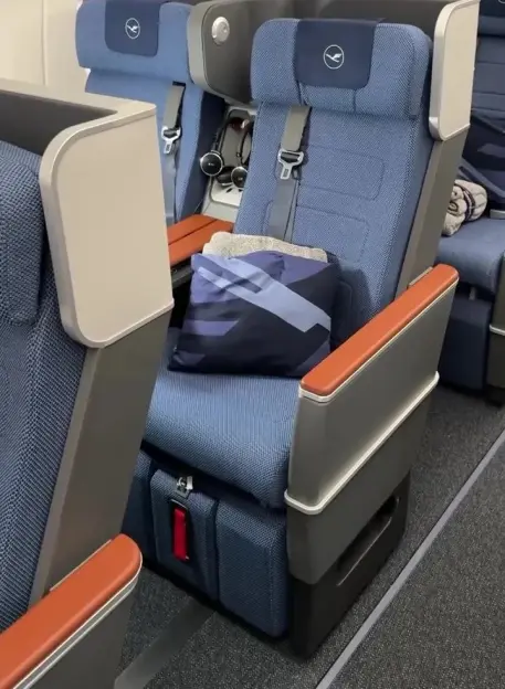Blue Lufthansa airline seats with headphones, pillow, and blanket.