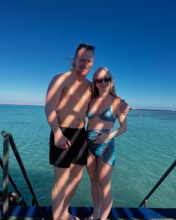 Couple in swimwear standing on a dock over turquoise water.