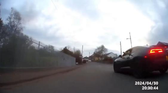 Rear view of a dark-colored car driving down a residential street.