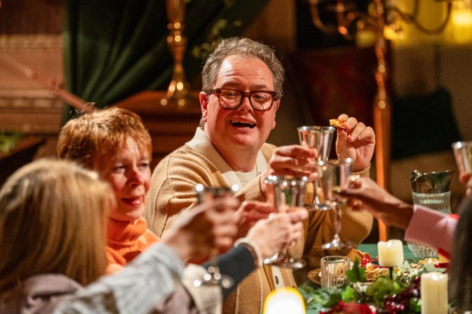 A group of people, including Alan Carr, cheering with silver goblets at a dinner table.