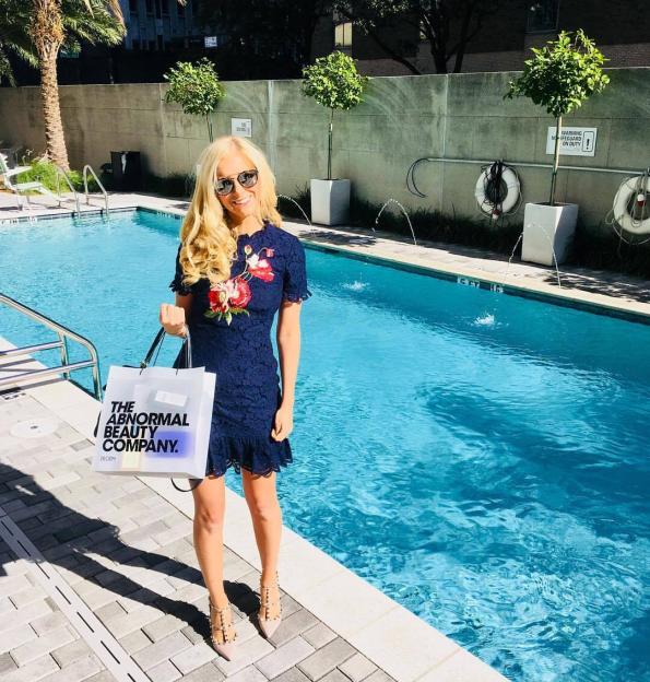 Woman by a pool holding a The Abnormal Beauty Company bag.