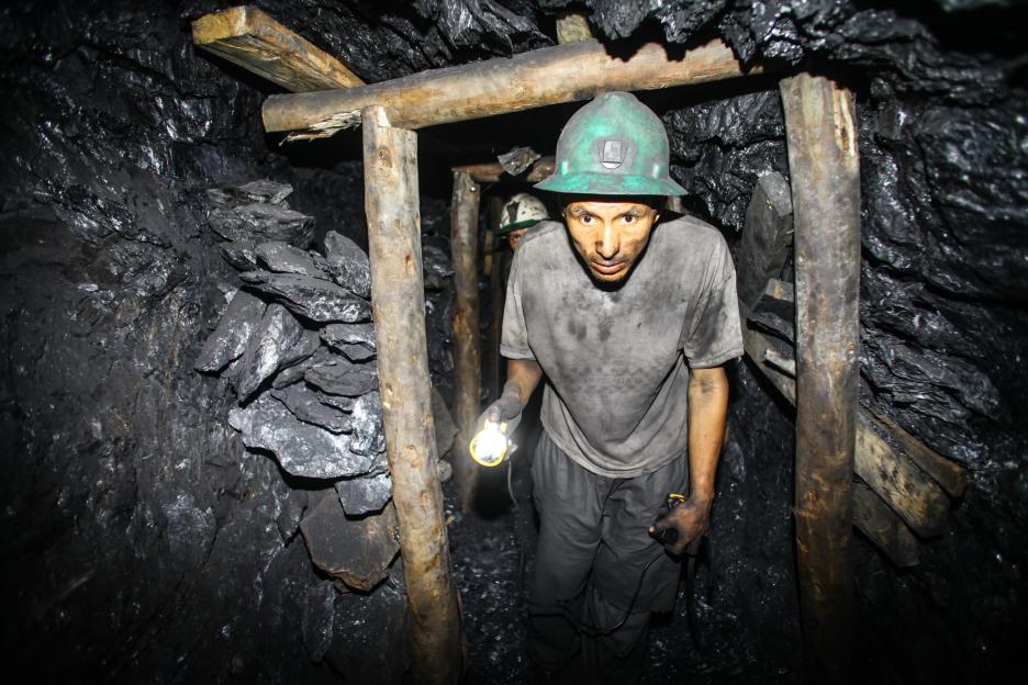 Miner with flashlight in dark gold mine.