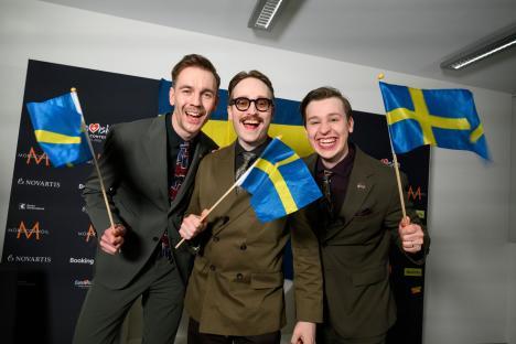 Three men in suits celebrating with Swedish flags.