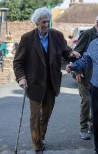 Tom Baker walking with friends using a cane.