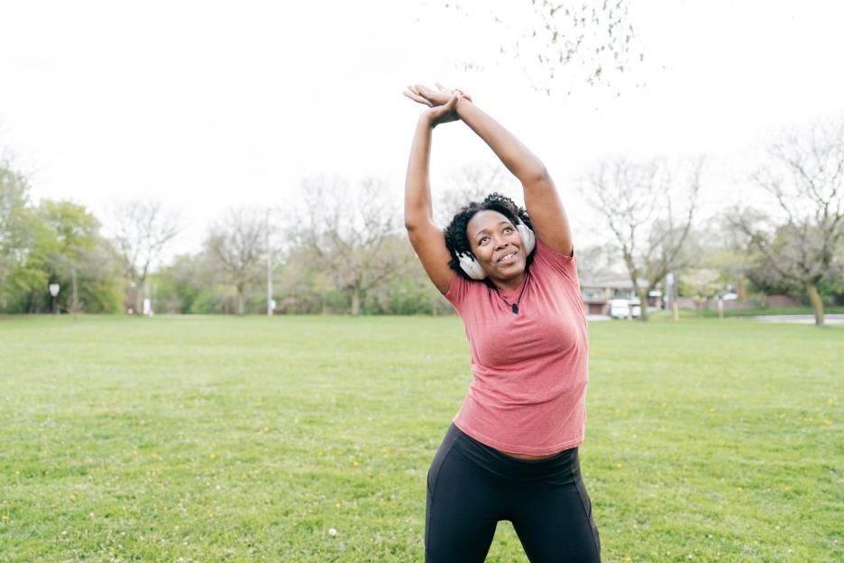 Woman stretching outdoors while wearing headphones.