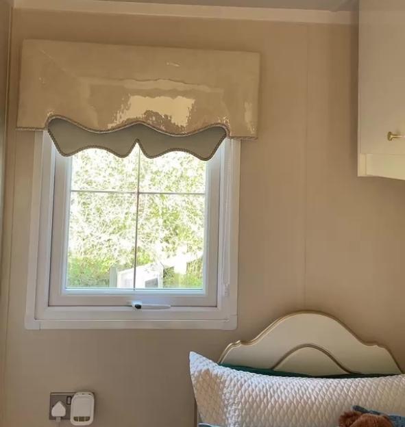 A beige window valance with scalloped edges above a window in a bedroom.