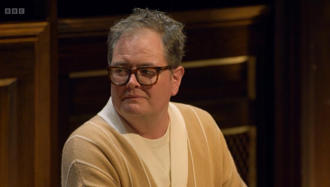 Alan Carr in a cream and beige striped cardigan, looking sideways.