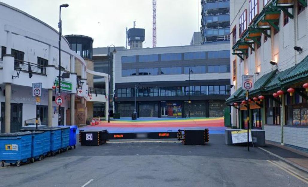 Street scene in Birmingham city centre with a rainbow-colored pedestrian area blocked by security barriers.
