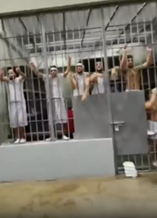 Inmates in white clothes shouting from behind bars in a prison.