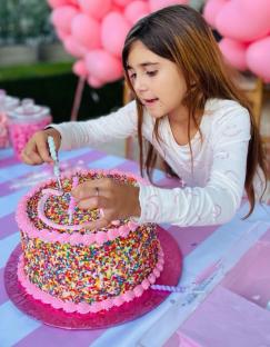 Girl placing candles on a sprinkle birthday cake.