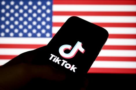 TikTok logo on a phone screen in front of a blurred US flag.