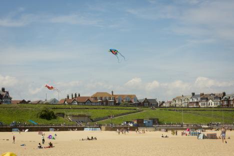 Beach scene with kites in the air and people enjoying the sand.