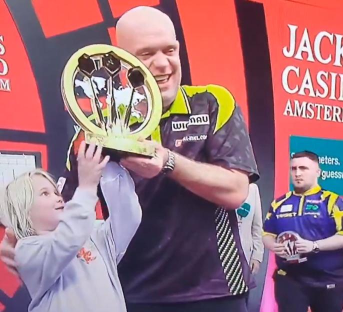 A man holds up a darts trophy while a child helps lift it.