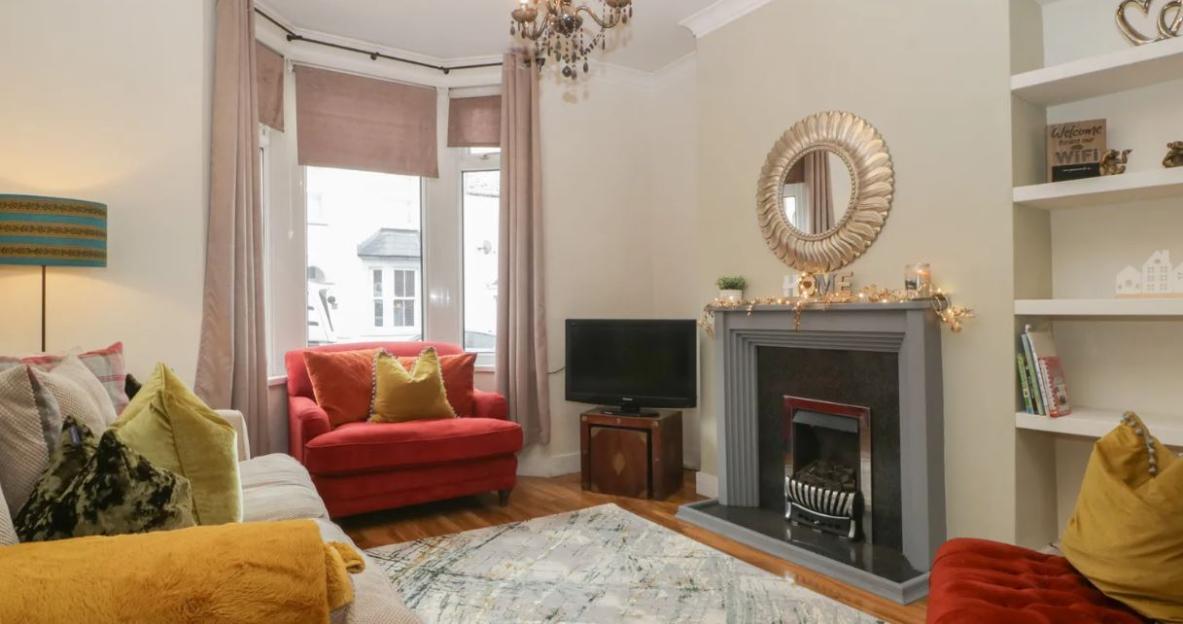 Living room of Lush House with a red armchair, fireplace, and mirror.