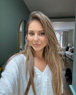 Woman with long brown hair wearing a white shirt.