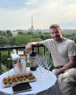 David Beckham on a balcony in Paris with wine and appetizers, the Eiffel Tower in the background.
