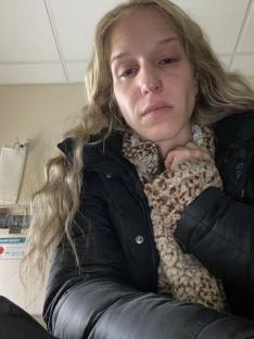 A woman with blonde hair sits in what appears to be a hospital room, looking distressed.