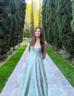 Woman in light blue gown walking down a garden path.