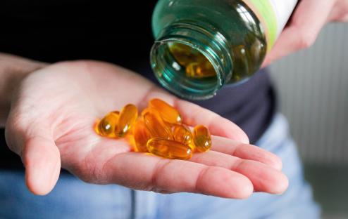 Hand holding several yellow flaxseed oil capsules poured from a bottle.