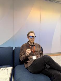 Man wearing smart glasses sits on a couch.