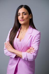 Portrait of a woman in a pink blazer with her arms crossed.