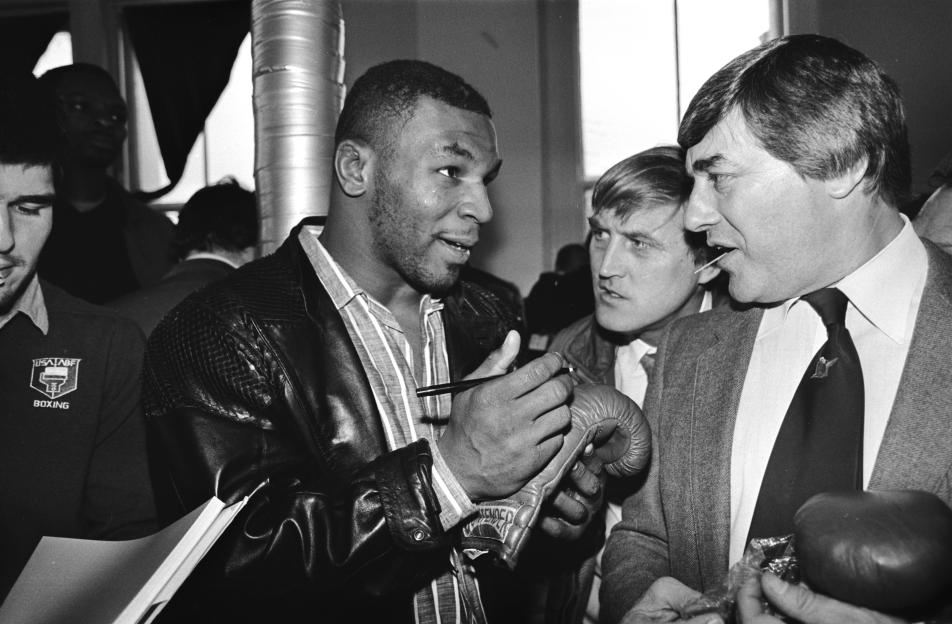 Mike Tyson signing a boxing glove for Frank Bruno at a London gym.
