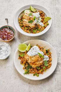 Two plates of spicy fish with rice, peas, chickpeas, and a yogurt sauce.