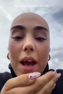 Close-up of a woman with short hair and decorated nails, blowing on her hands to avoid ruining her manicure.