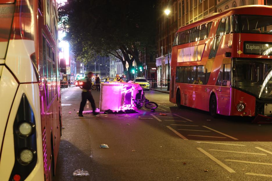 A damaged rickshaw and London bus at a crash scene at night.