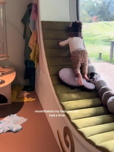 Toddler climbing a soft play structure next to a large window.