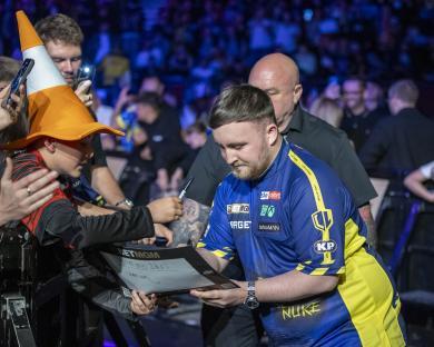 Luke Littler signing an autograph for a fan.