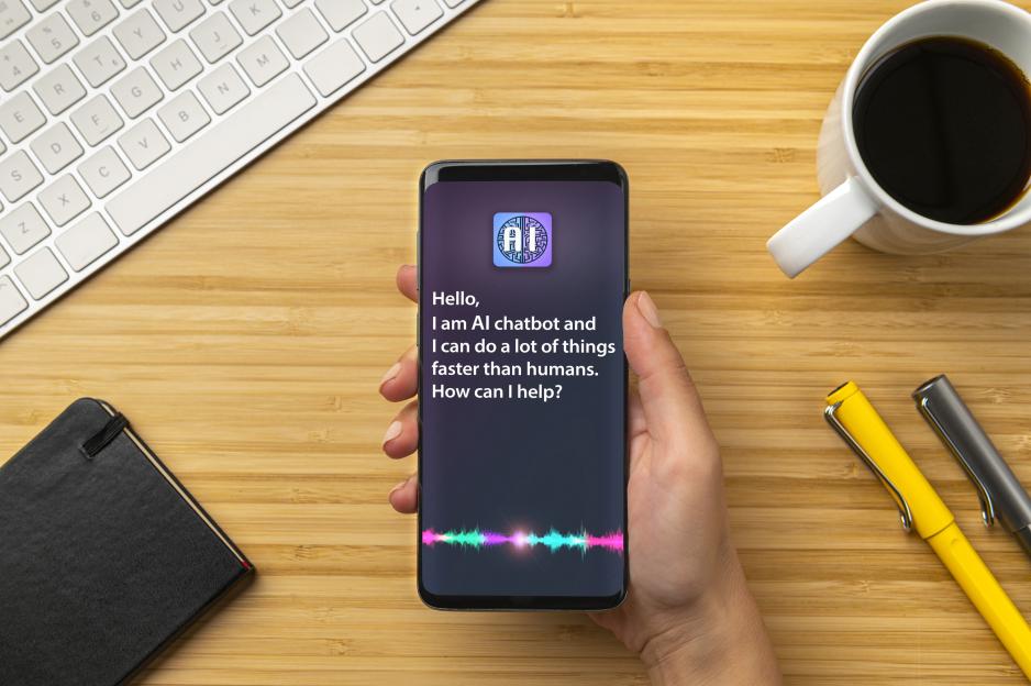 Hand holding a smartphone displaying an AI chatbot that says, "Hello, I am an AI chatbot, and I can do many tasks faster than humans. How can I assist you?"