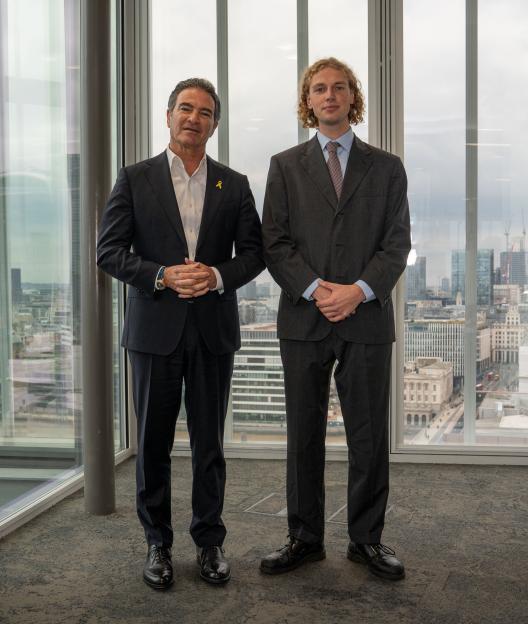 Yossi Cohen, former head of Mossad, and Sun reporter Patrick Harrington standing in front of a window with a city skyline view.